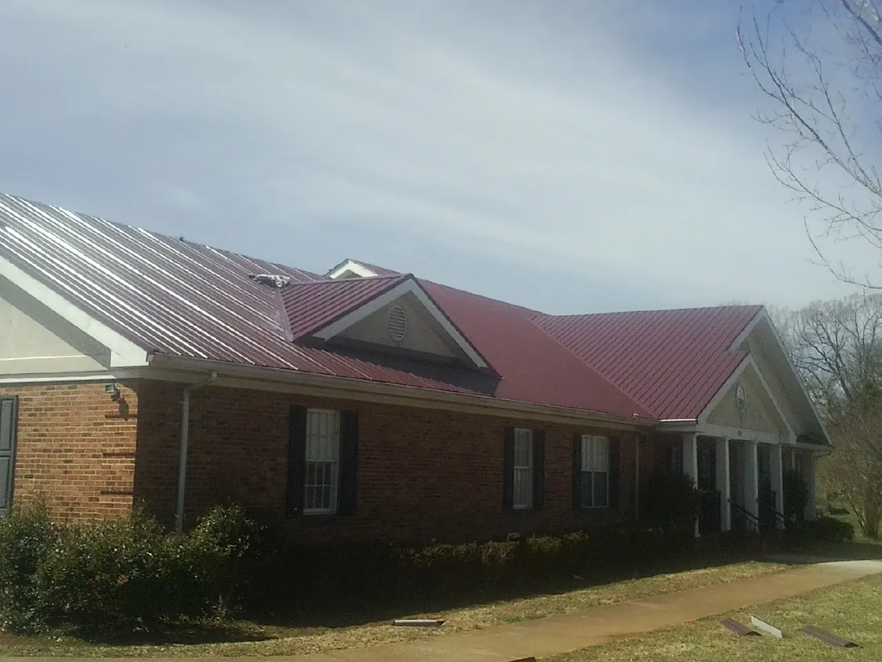 Red metal roof with gabled entries on a long brick building, from a Hail Damage Roof Repair job in Chicopee