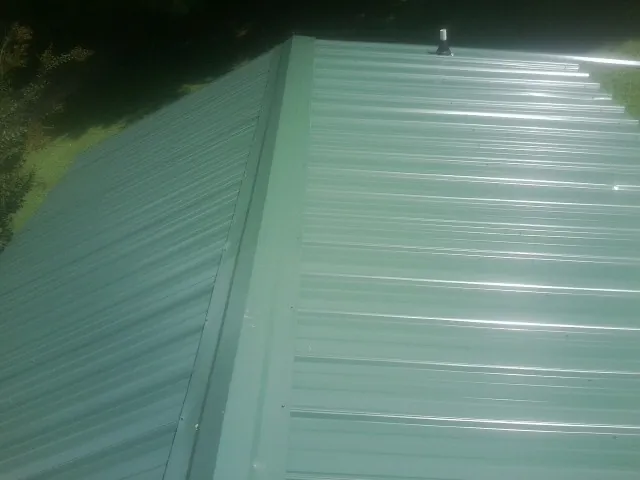 New green metal panels meeting at the ridge of a roof — Flat Roof Repair work by our crew in Chicopee