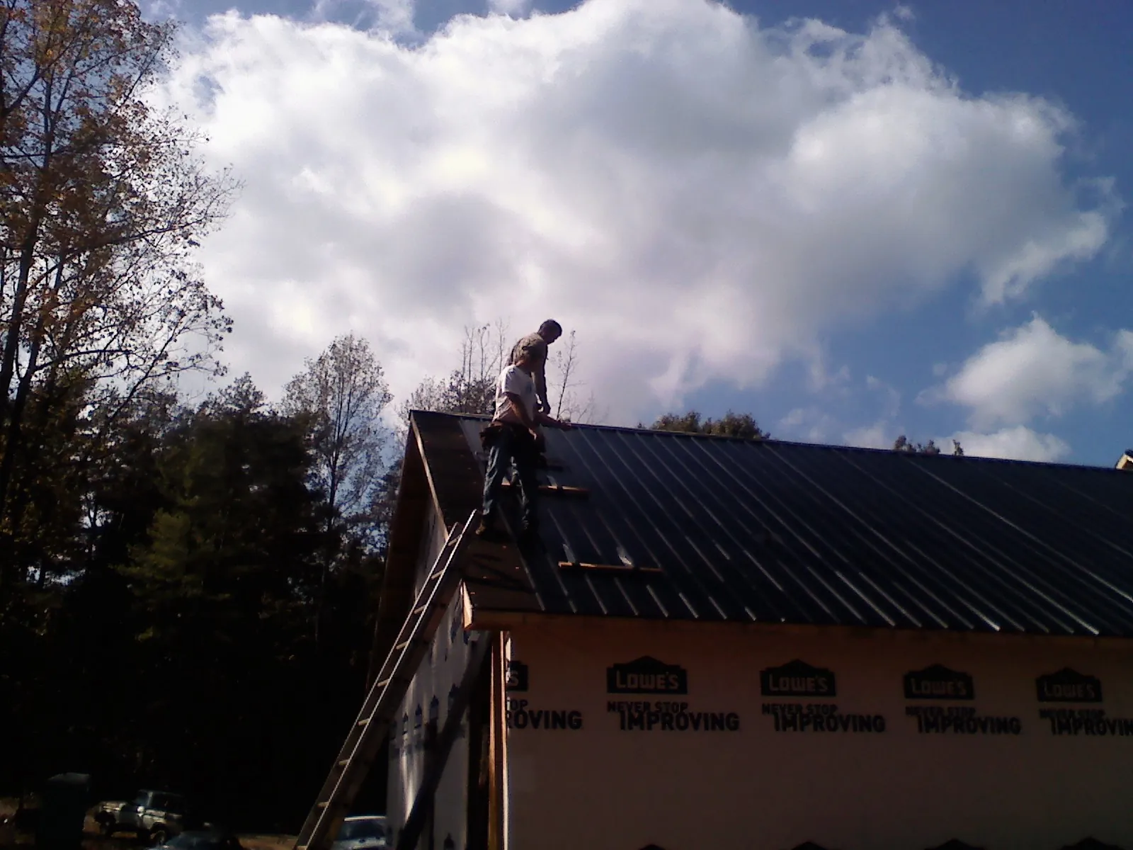 Roofer fastening dark metal panels high against a cloudy sky, from a Roof Inspection job in Chicopee