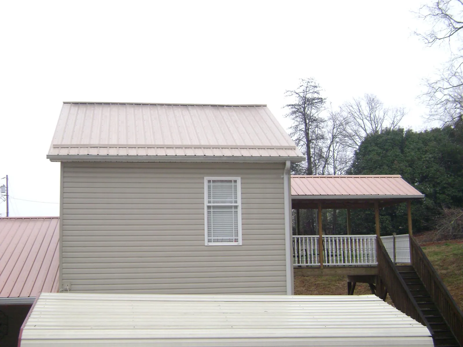 Tan metal roofs on a two story addition and attached porch, from a Roof Replacement job in Chicopee